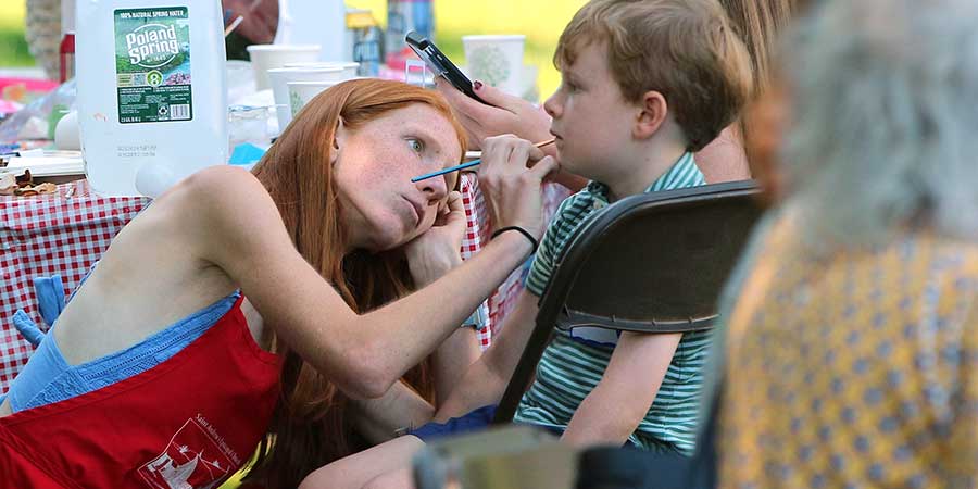 Young woman painting face of boy at picnic